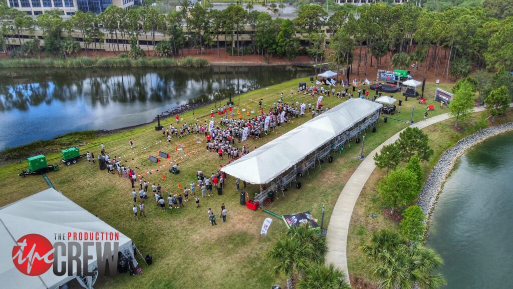 Aerial view of an outdoor corporate event near a scenic pond in Florida, featuring tents, attendees, and activity zones, organized by a professional event crew.
