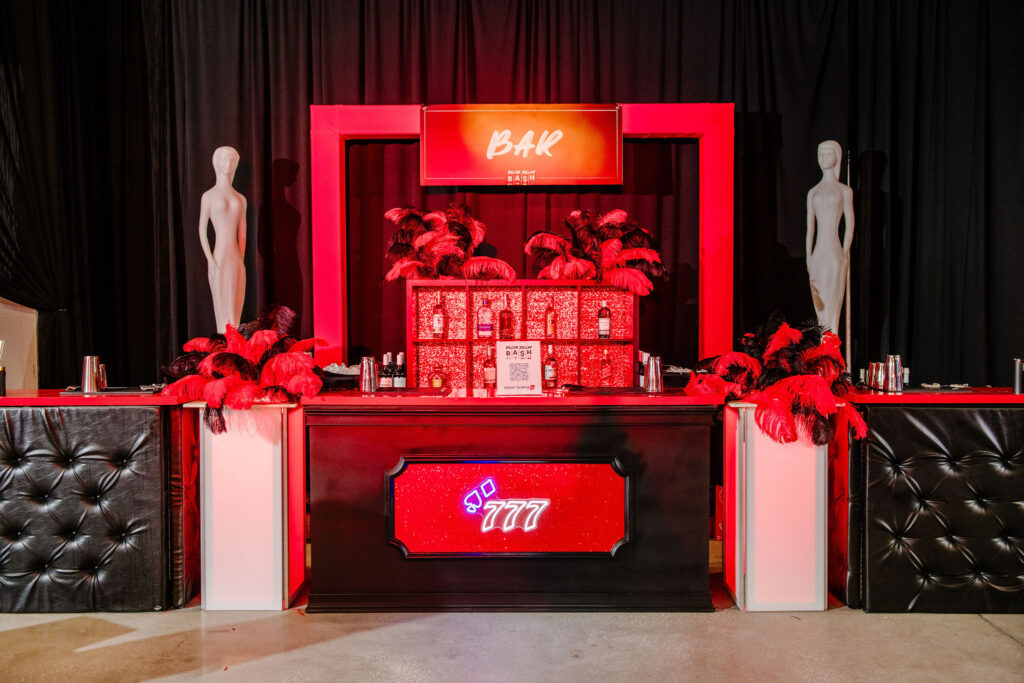 Luxurious bar setup with red and black decor, adorned with feather arrangements and mannequins, ideal for a high-end party or gala.