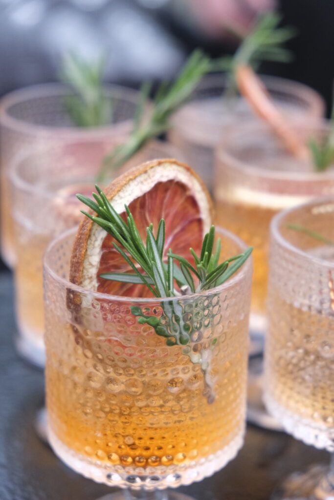 Close-up of a beautifully garnished cocktail with a rosemary sprig and dried blood orange slice, perfect for a stylish banquet or party