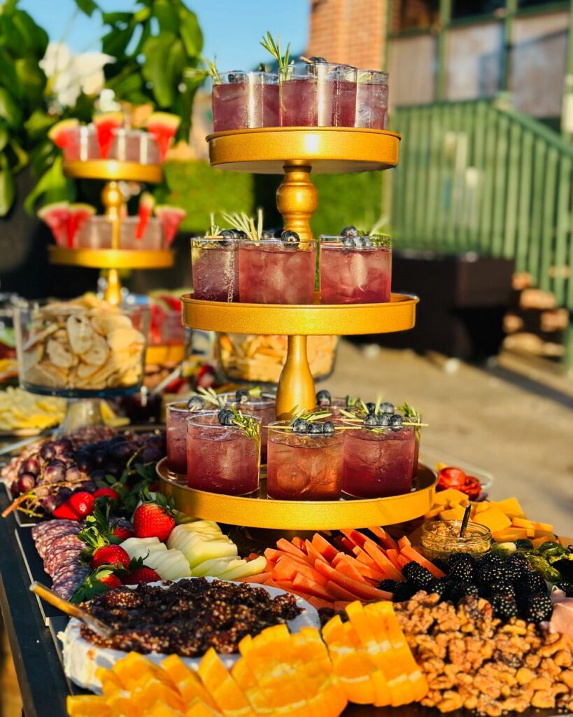 Three-tiered golden tray with blueberry cocktails and a variety of fresh fruits and charcuterie, catering setup by UDREAM EVENTS in St. Petersburg, Florida