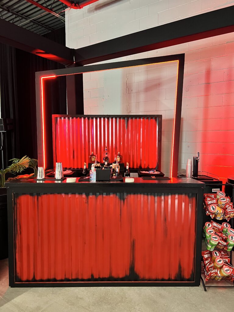 Bold red neon bar with corrugated metal design, creating a striking focal point at an industrial-themed event.