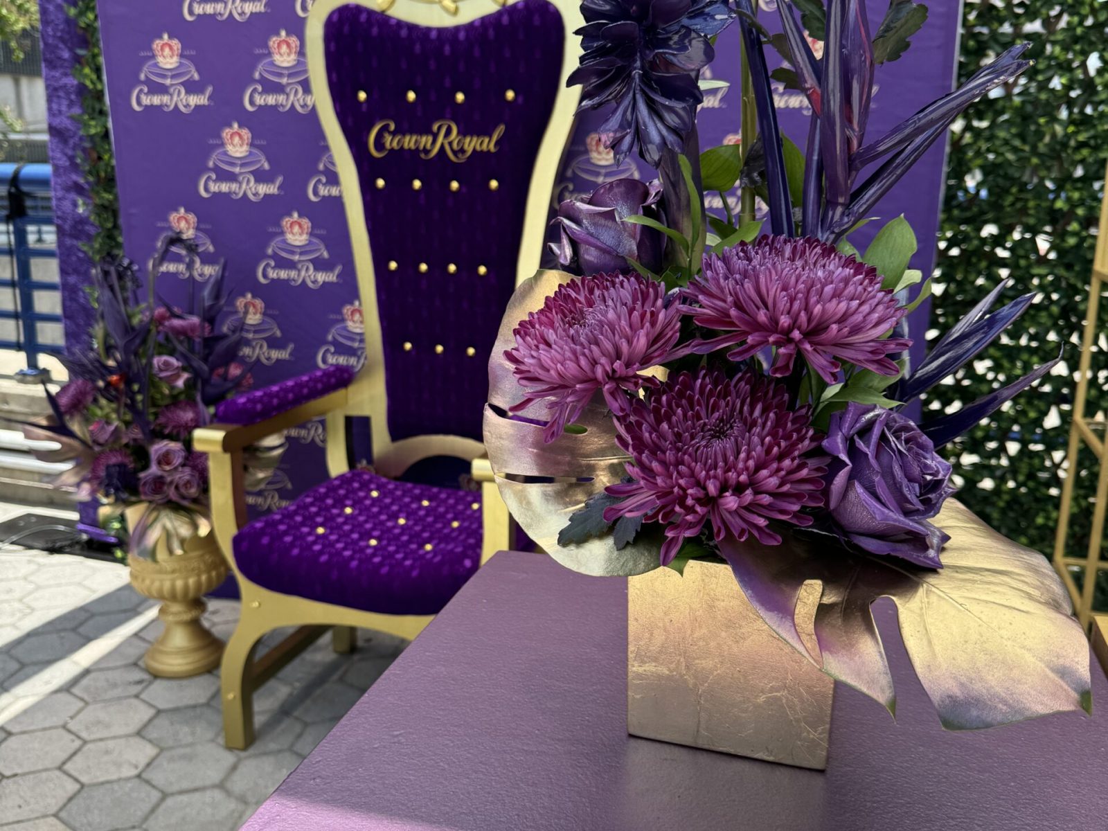 Crown Royal-themed setup with a regal purple and gold chair, complemented by purple floral arrangements, styled by UDREAM EVENTS for a luxurious event display.