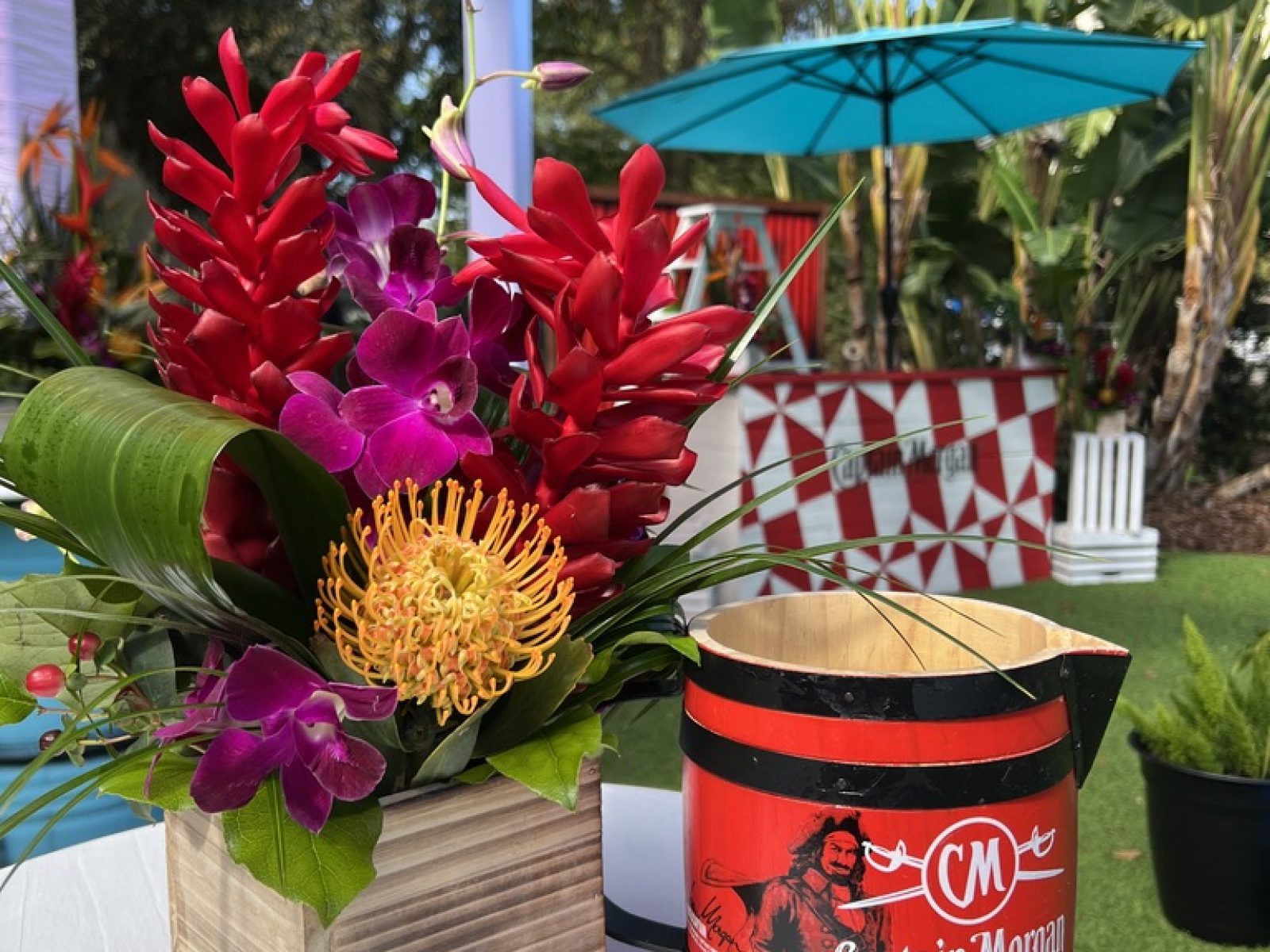 Close-up of a floral centerpiece with vibrant red and purple flowers next to a Captain Morgan-branded barrel at an event in Tampa Bay, styled by UDREAM EVENTS