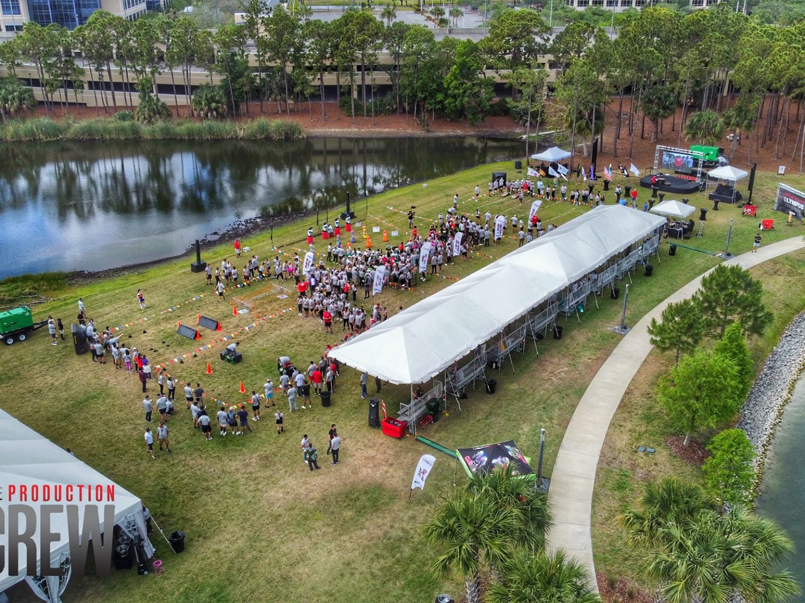 Aerial view of an outdoor corporate event near a scenic pond in Florida, featuring tents, attendees, and activity zones, organized by a professional event crew.