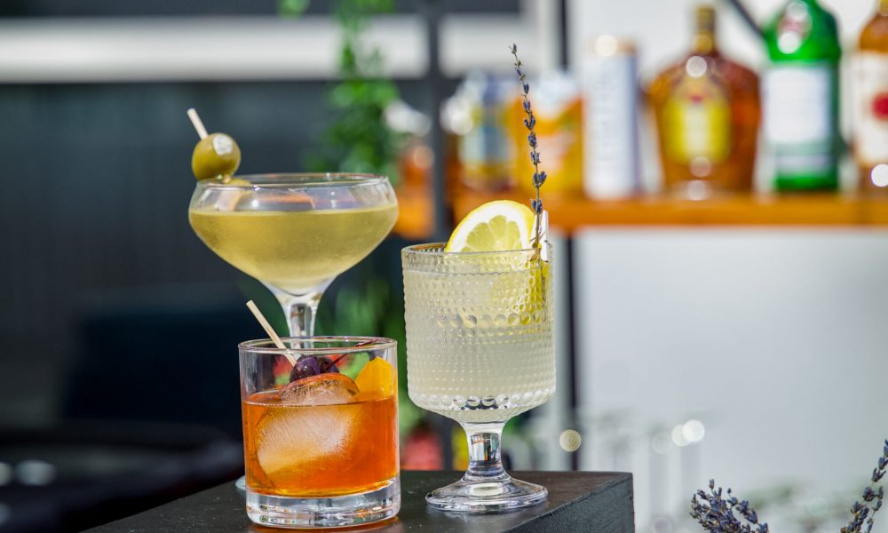 Assorted cocktails elegantly displayed on a black pedestal, featuring a martini, old fashioned, and gin fizz, perfect for a sophisticated party or corporate event.