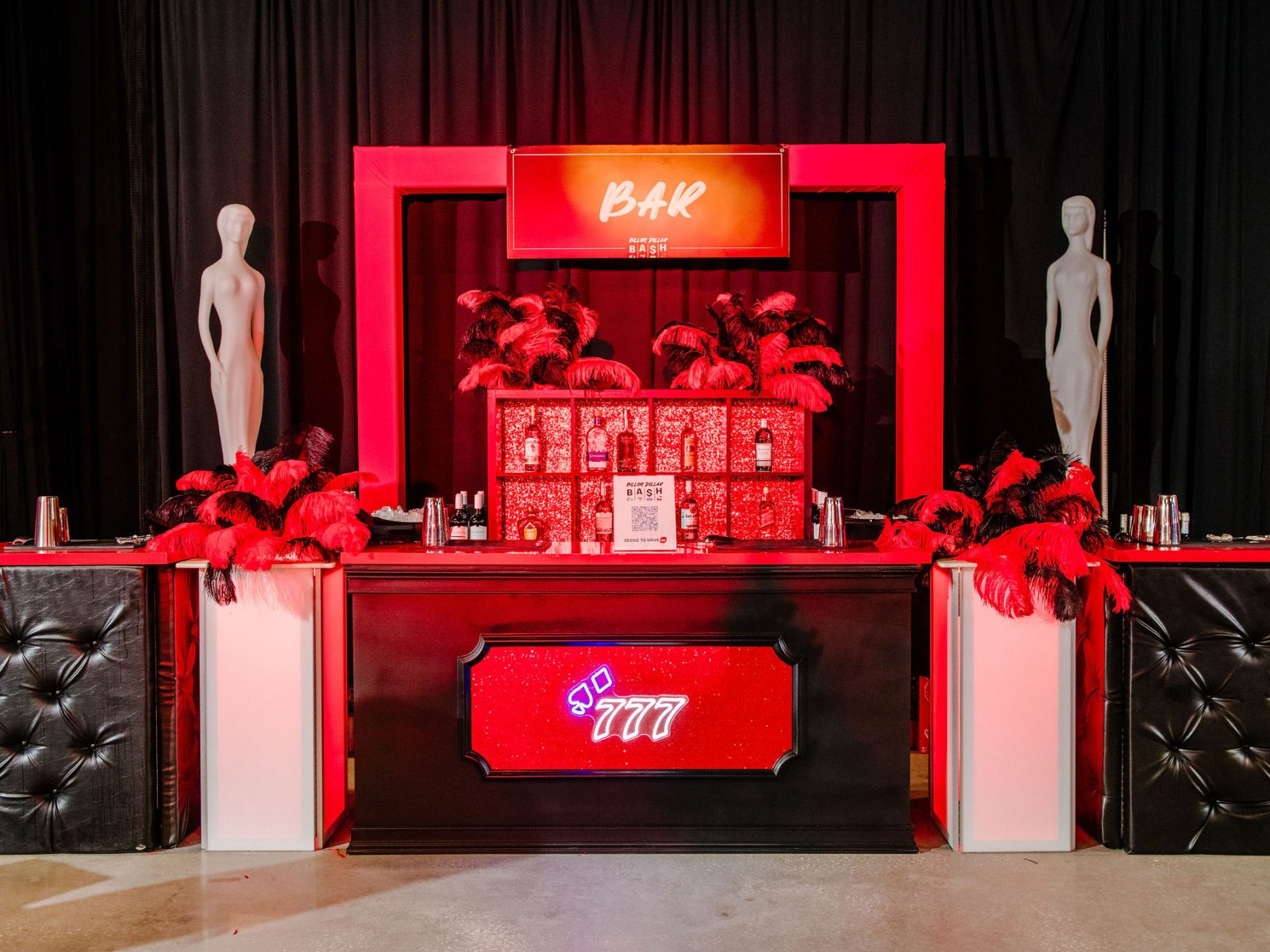 Luxurious bar setup with red and black decor, adorned with feather arrangements and mannequins, ideal for a high-end party or gala.