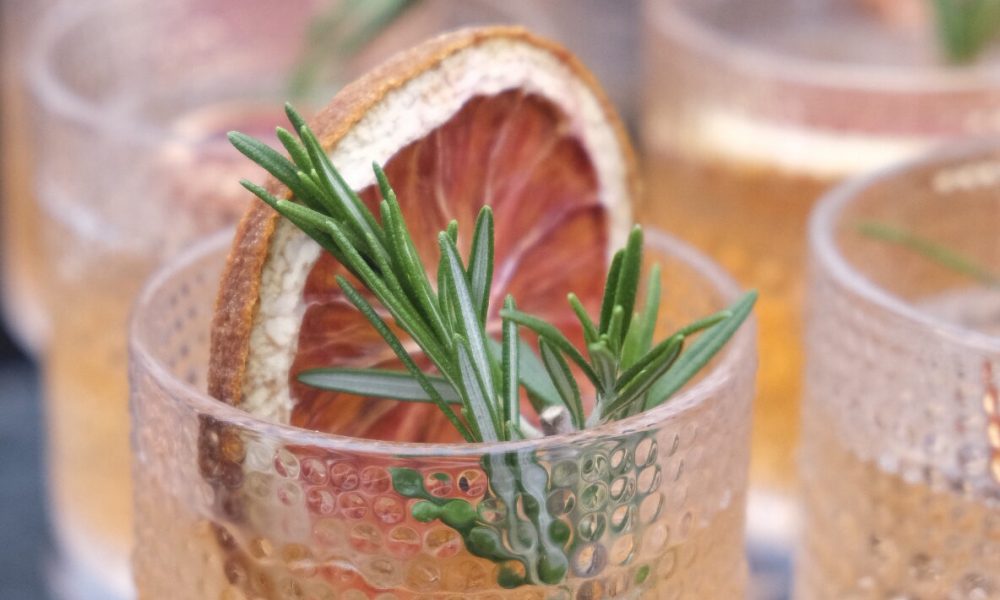 Close-up of a beautifully garnished cocktail with a rosemary sprig and dried blood orange slice, perfect for a stylish banquet or party