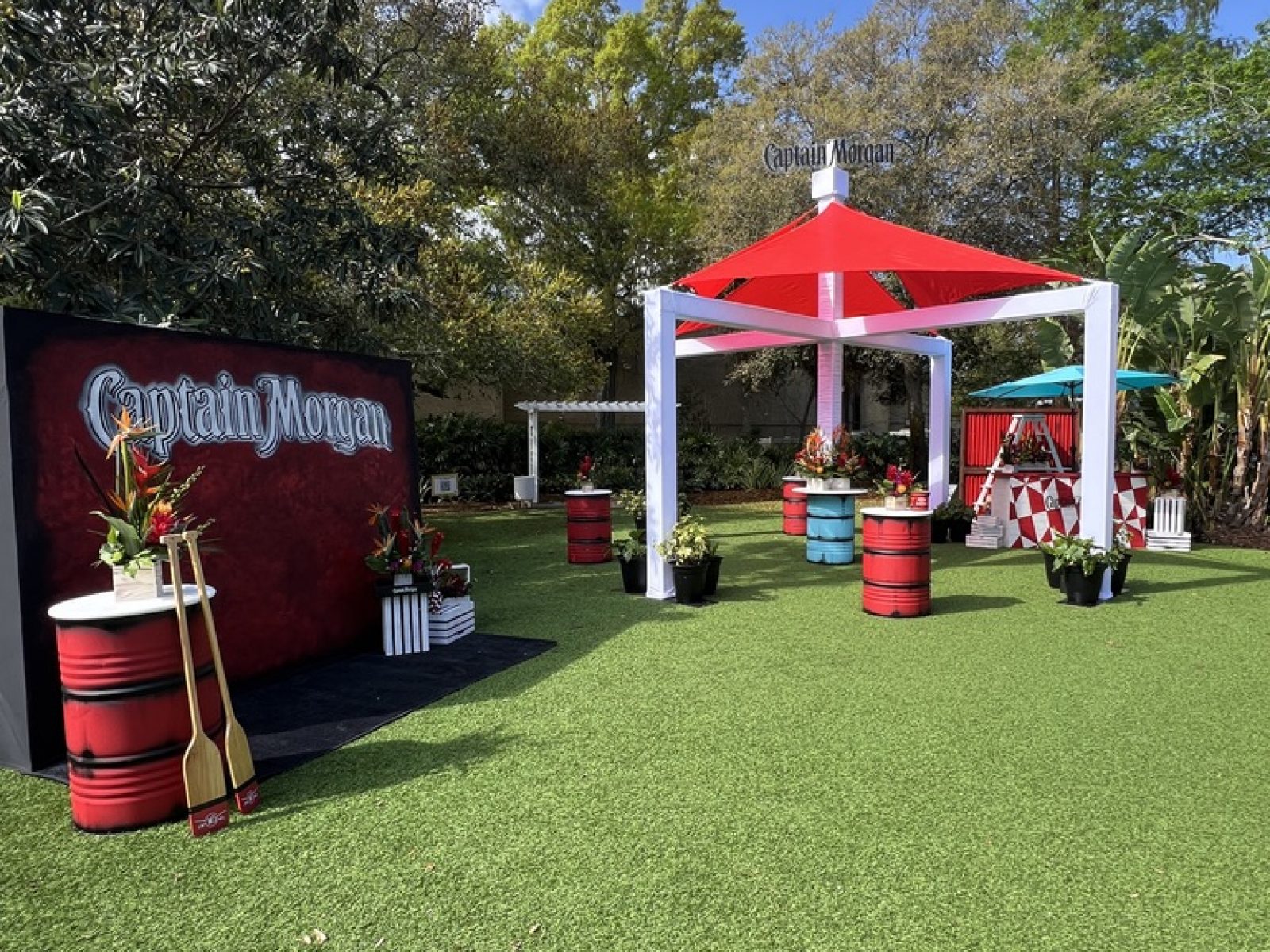 Vibrant Captain Morgan event space on Florida’s Gulf Coast, showcasing red and white themed canopies, decorative barrels, and tropical plants, set up by UDREAM EVENTS