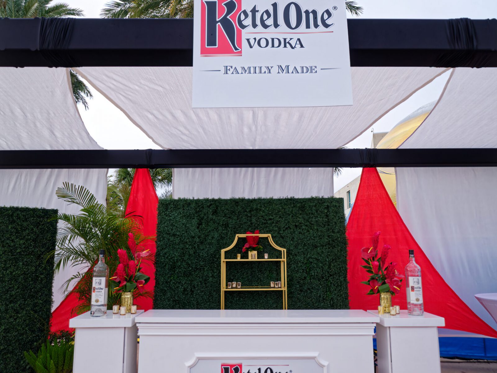 Ketel One Vodka event bar with elegant red and white decor, surrounded by greenery and branded signage, set up by UDREAM EVENTS for an outdoor event on Florida’s Gulf Coast.