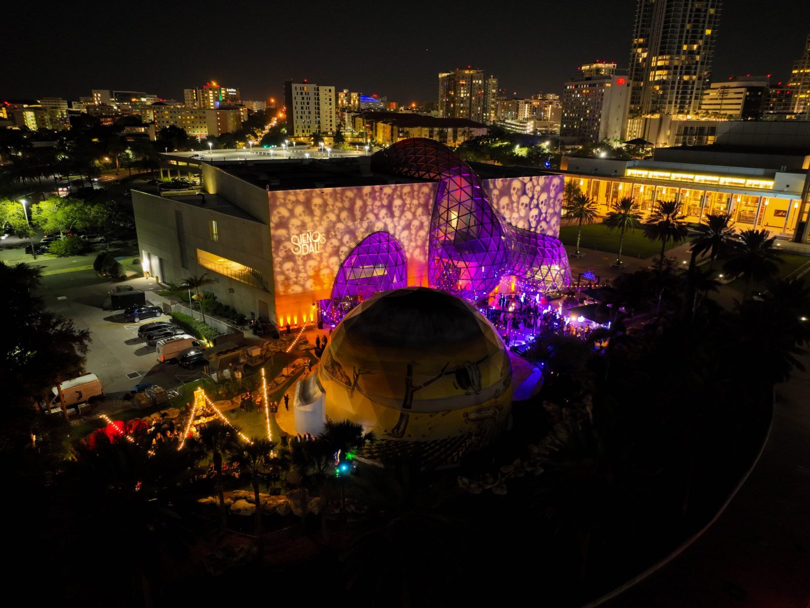 Aerial night view of a vibrant event at the Dalí Museum in St. Petersburg, showcasing colorful lighting and the city skyline.