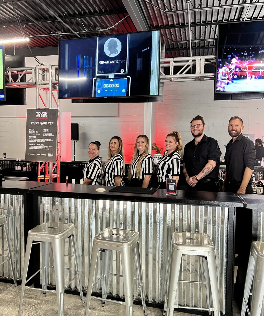 Bar staff dressed in referee shirts behind a sleek industrial bar setup, adding a playful theme to the corporate event.