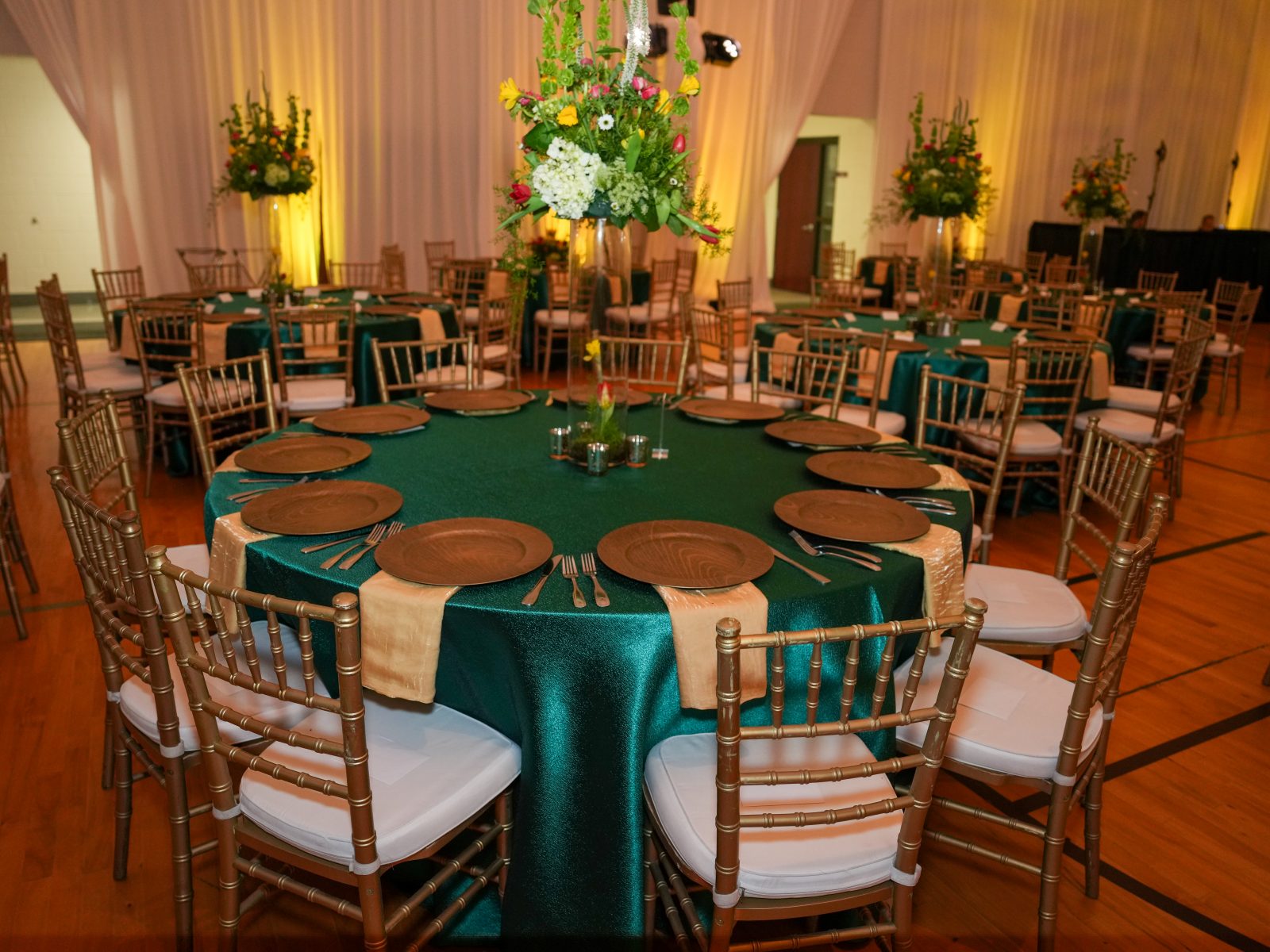 Formal dinner arrangement with round tables, green tablecloths, and elegant floral centerpieces, designed for a high-end event or celebration.