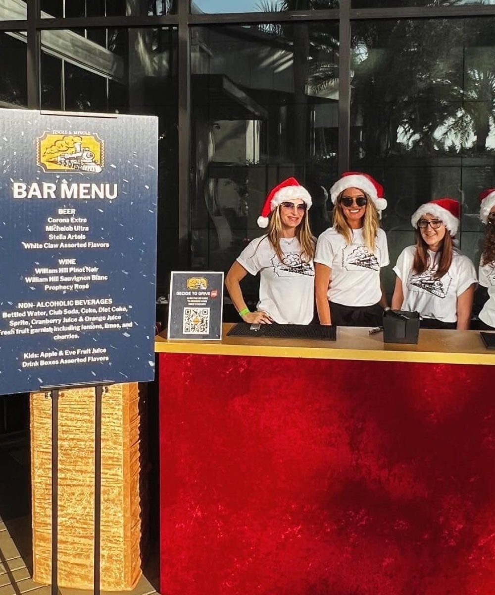 Festive bar setup with four bartenders in Santa hats, offering a cheerful holiday bar service at a Florida venue.